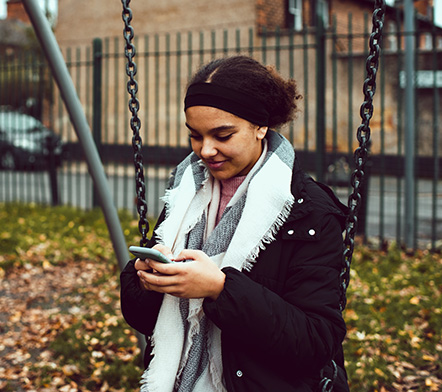 young carer using her mobile sitting on a swing